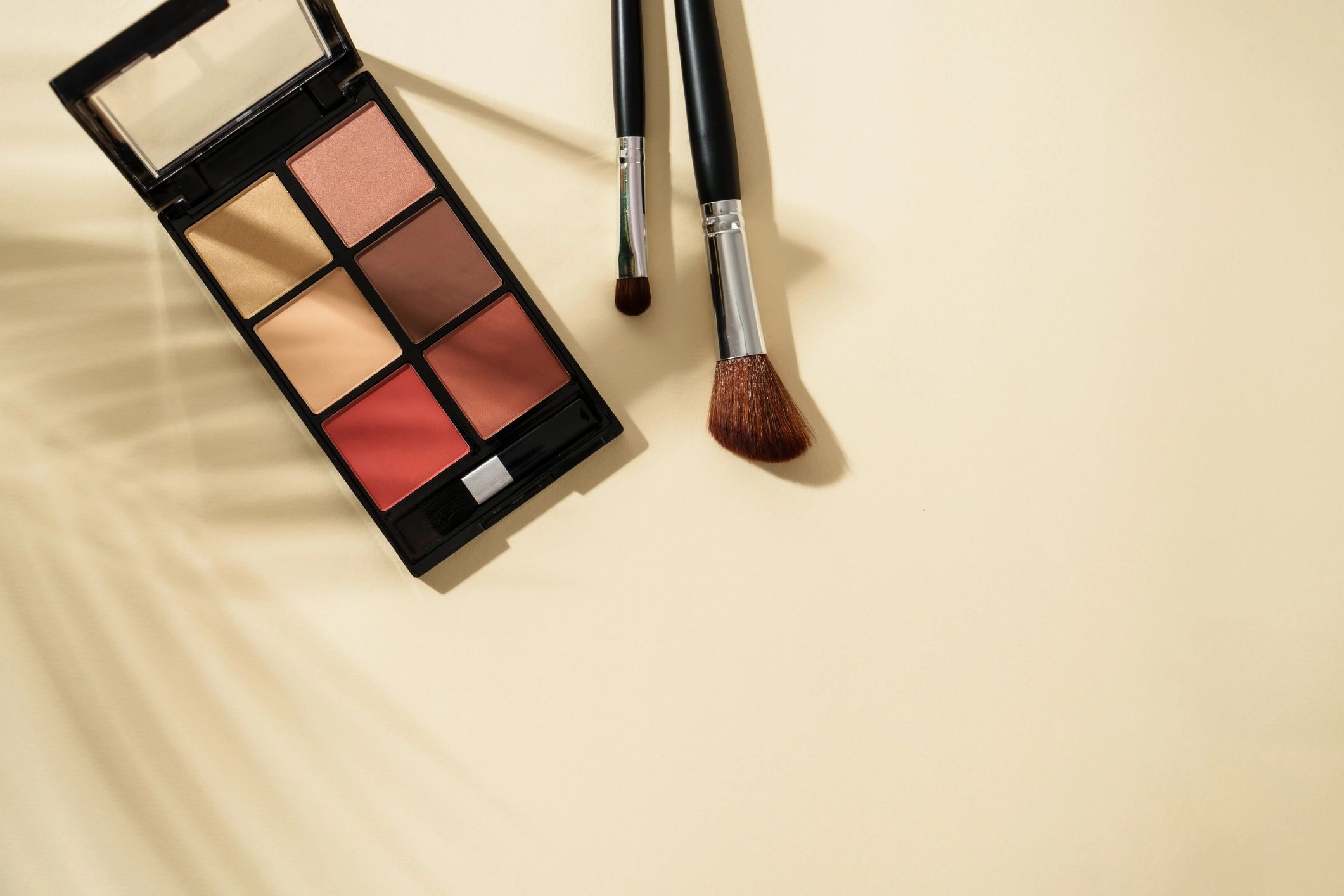 Makeup palette and brushes on pastel background
