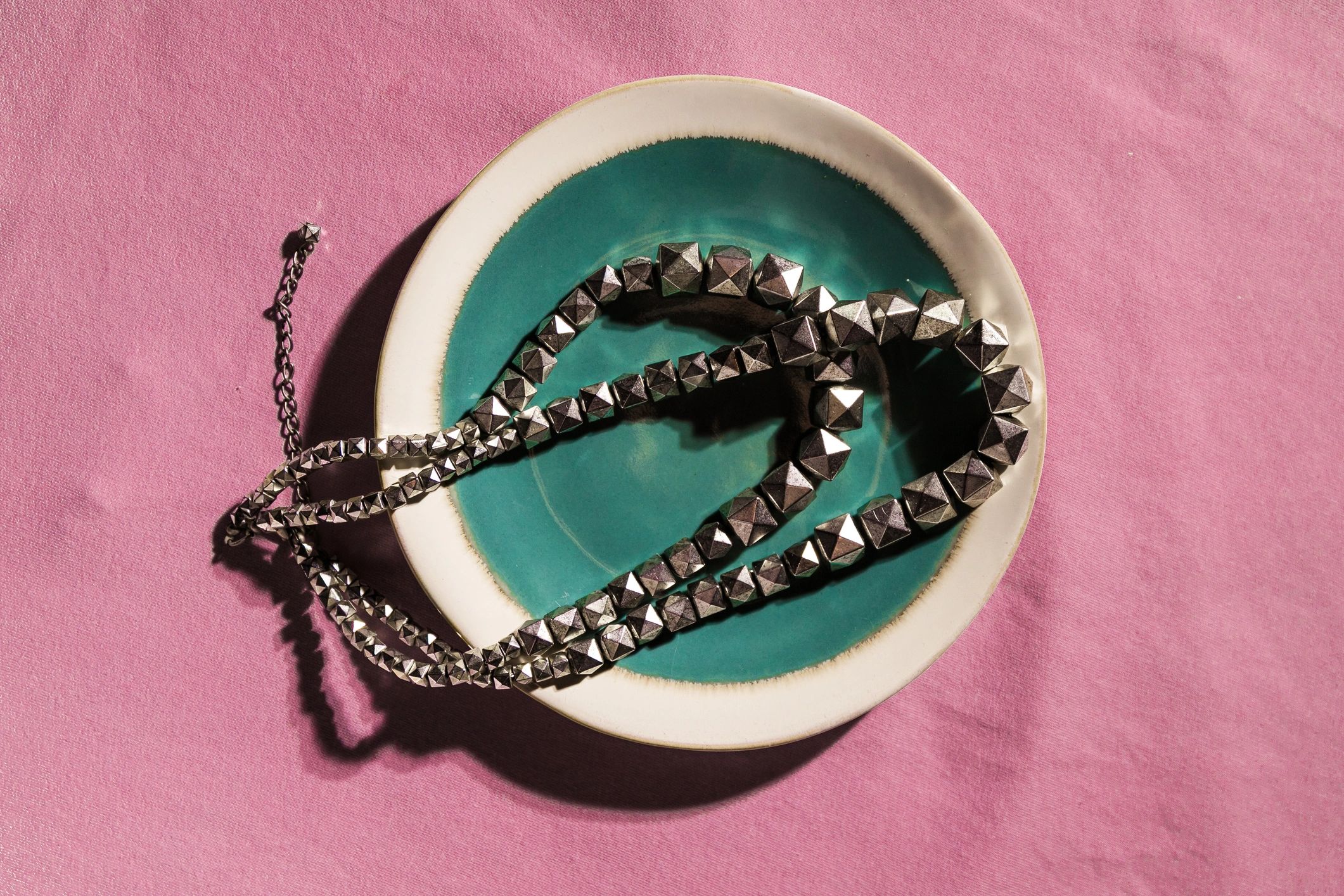 Silver chain in ceramic bowl on pink fabric