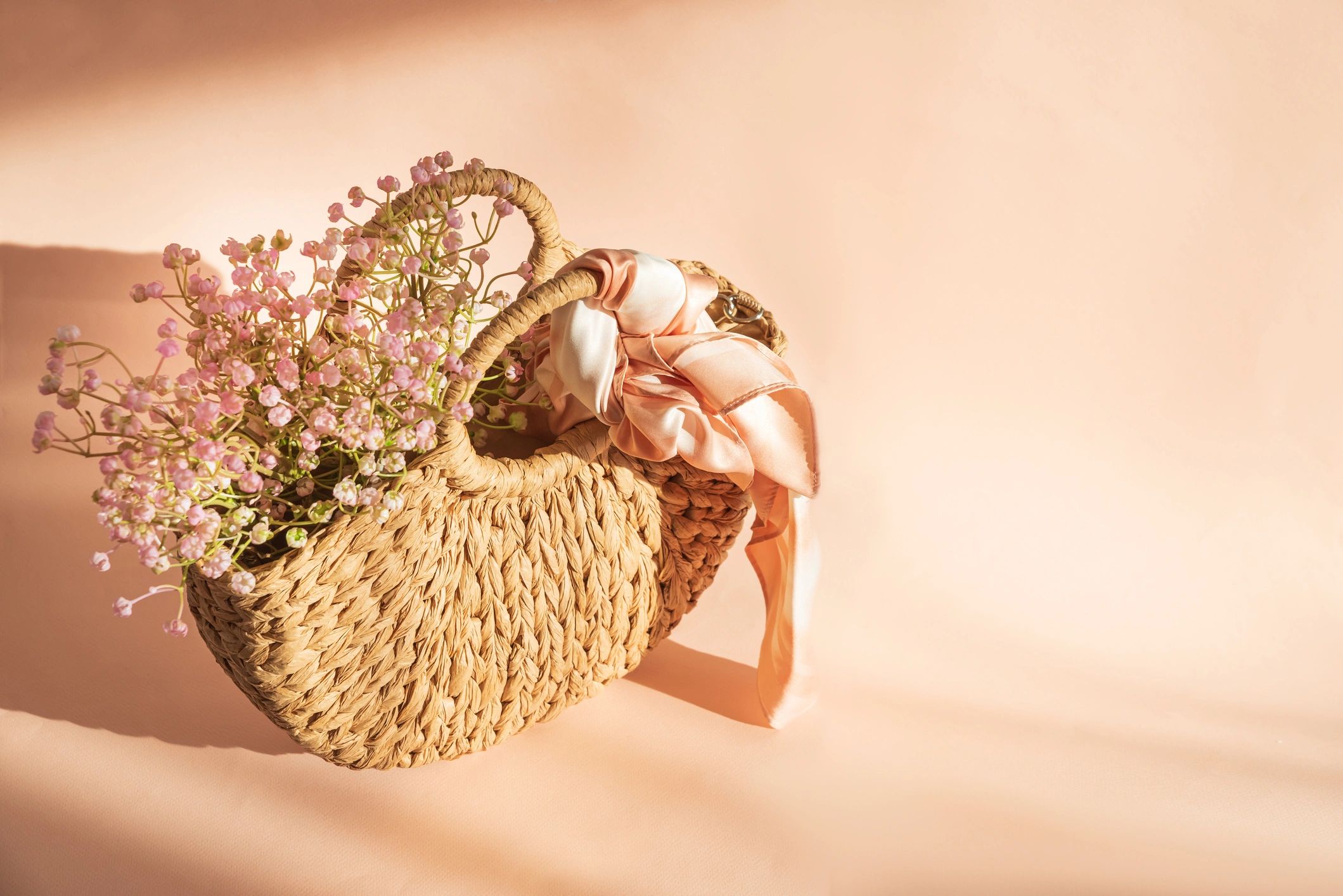 Straw handbag and flowers on pink background